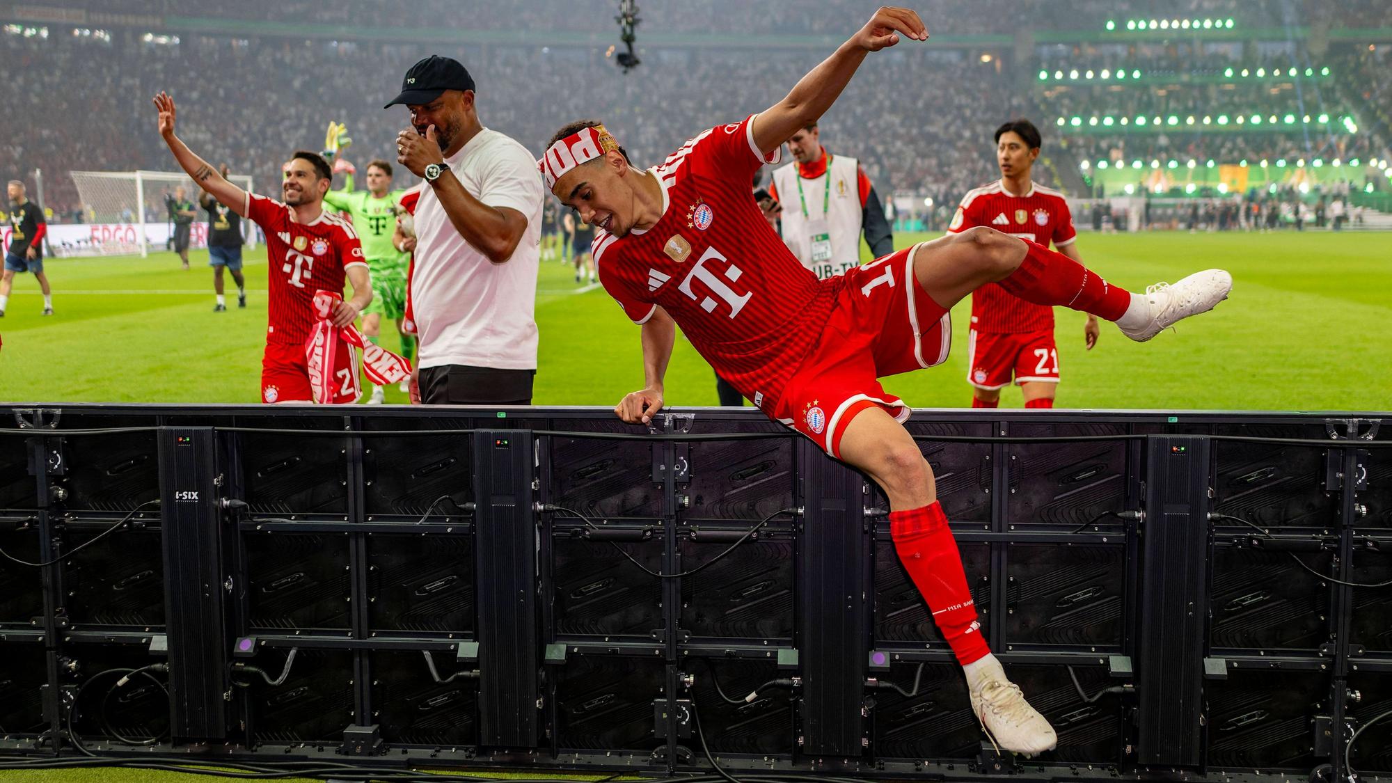 Bayerns Jamal Musiala klettert nach dem Pokalsieg über die Bande im Olympiastadion.