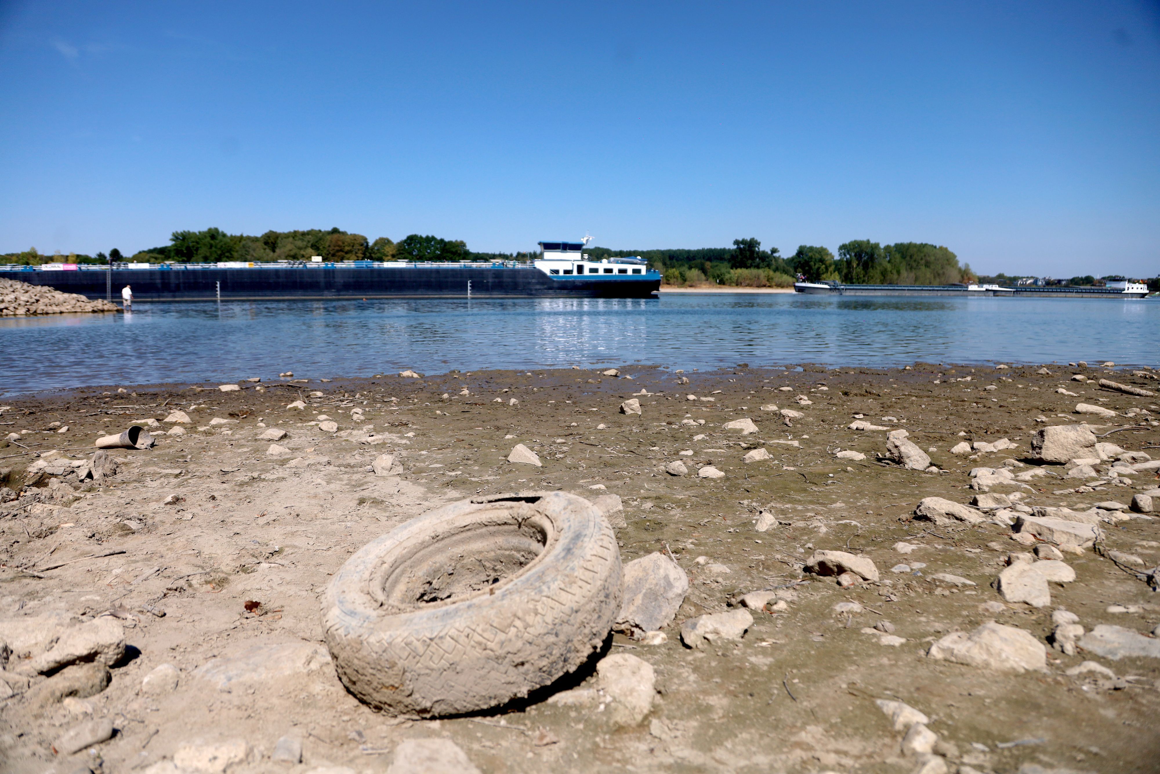 Der sinkende Rheinpegel hat einen Autoreifen trockengelegt, im Hintergrund ist ein Schiff im Rhein unterwegs.