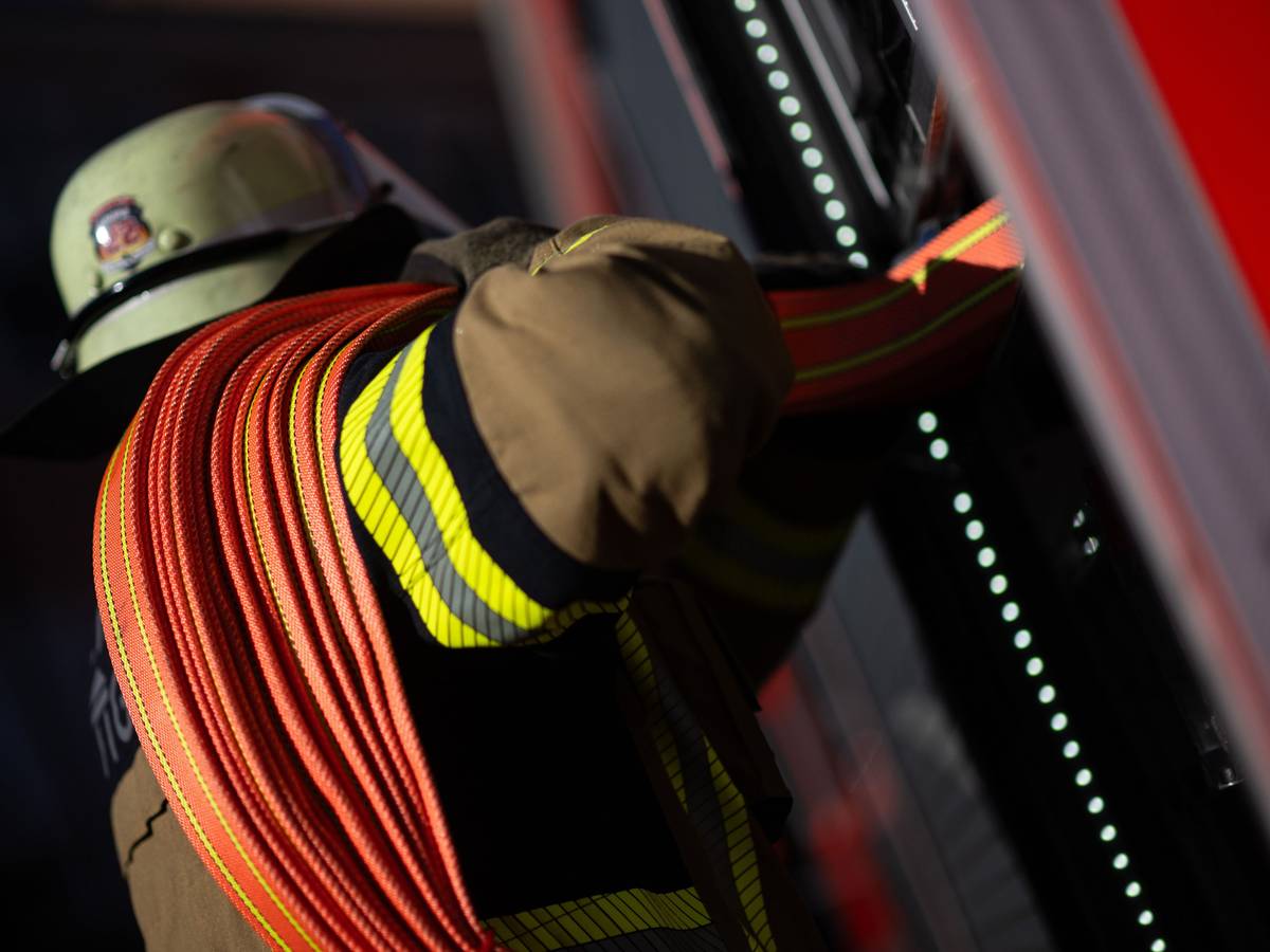 Eine Einsatzkraft der Feuerwehr nimmt einen Schlauch aus einem Einsatzfahrzeug der Feuerwehr. (Symbolfoto)