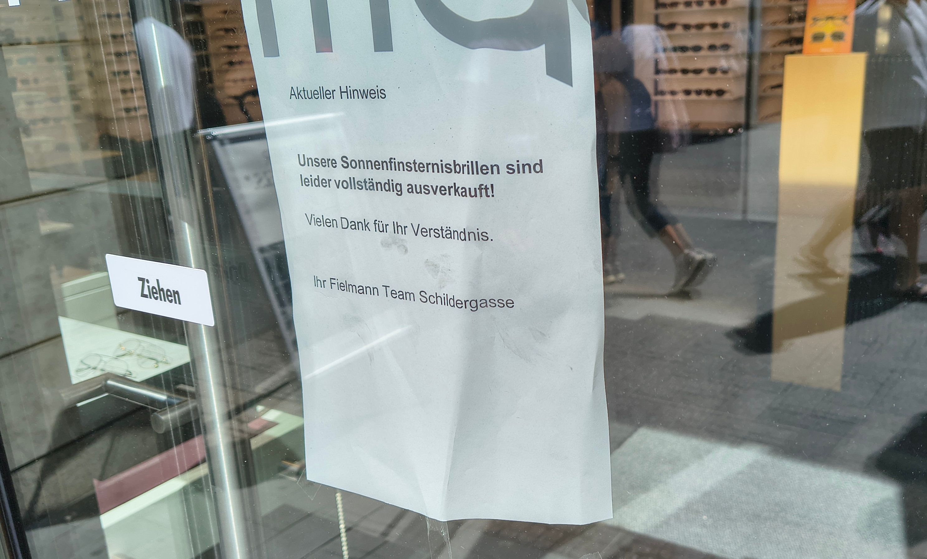 An der Tür eines Optikergeschäfts in der Kölner Innenstadt steht ein Schild mit der Aufschrift „Unsere Sonnenfinsternisbrillen sind leider vollständig ausverkauft!“.