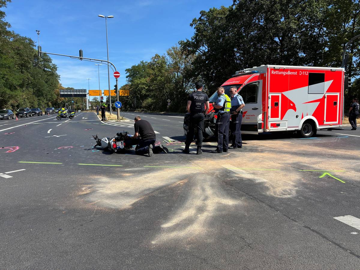 Vor einem RTW liegt ein Motorrad auf der Fahrbahn, Polizisten stehen davor, einer kniet.