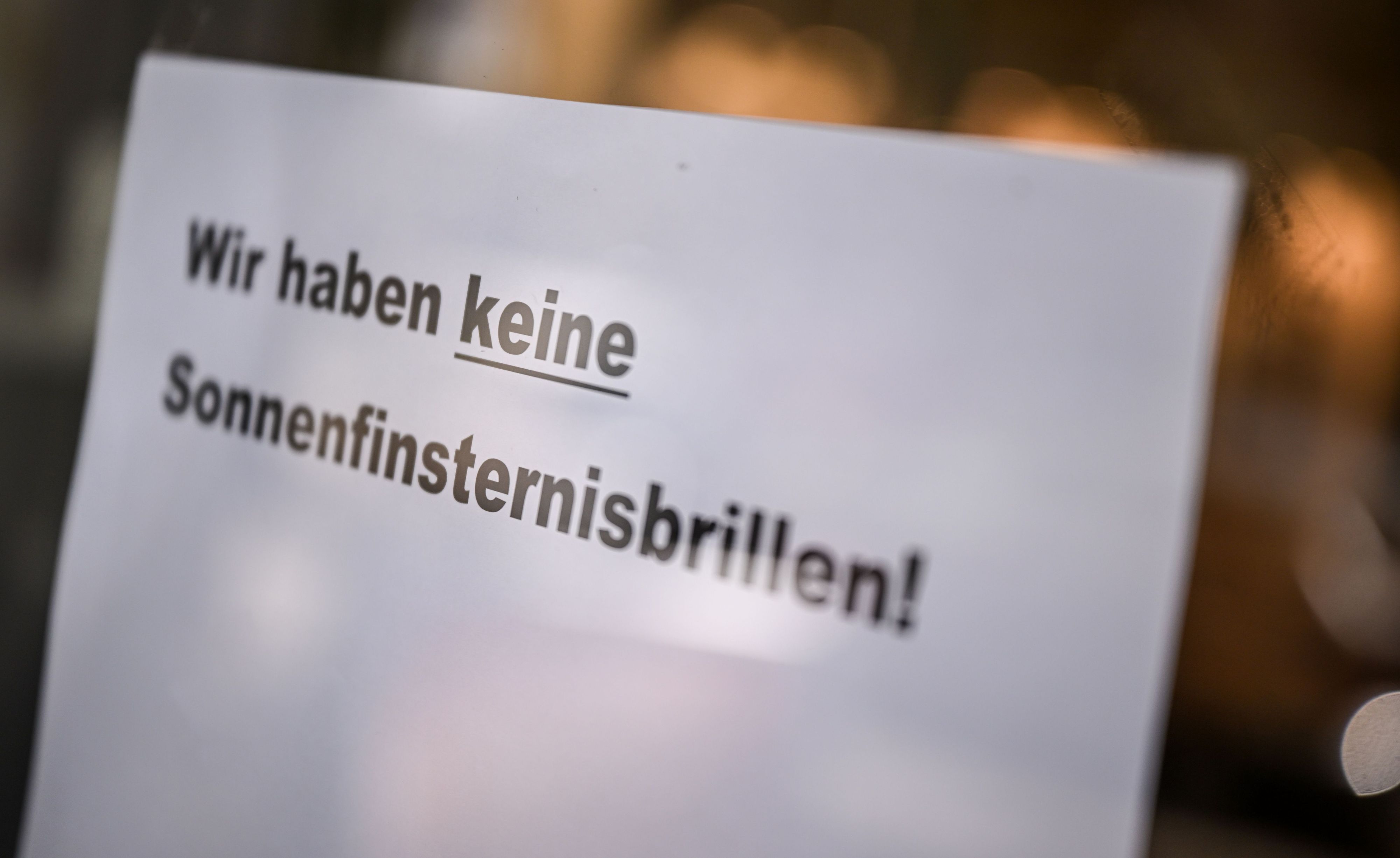 An der Tür eines Optikergeschäfts steht ein Schild mit der Aufschrift „Wir haben keine Sonnenfinsternisbrillen!“.