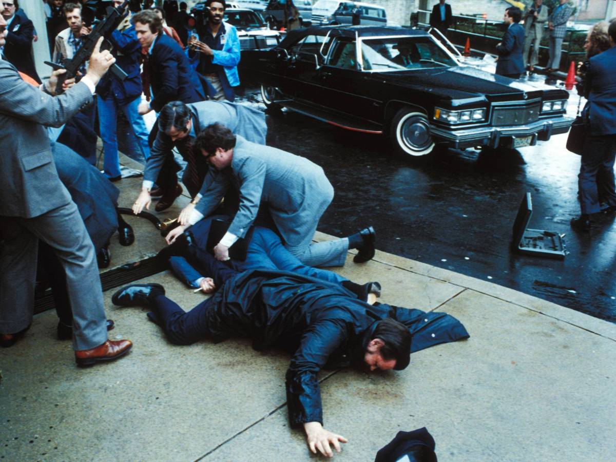 Unmittelbar nach den Schüssen auf US-Präsident Ronald Reagan überwältigen Sicherheitskräfte den Attentäter John Hinckley Jr. vor dem Washington Hilton Hotel, während der schwer verletzte Regierungssprecher James Brady und ein Polizist am Boden liegen.