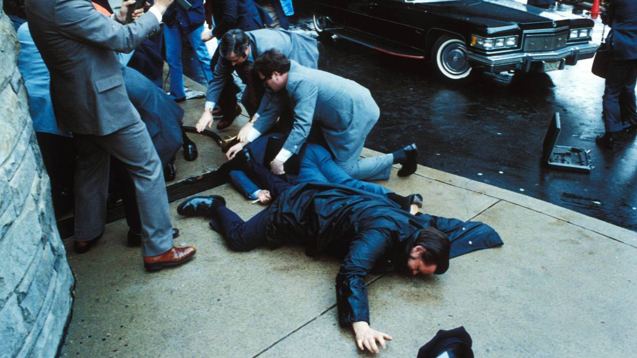 Unmittelbar nach den Schüssen auf US-Präsident Ronald Reagan überwältigen Sicherheitskräfte den Attentäter John Hinckley Jr. vor dem Washington Hilton Hotel, während der schwer verletzte Regierungssprecher James Brady und ein Polizist am Boden liegen.