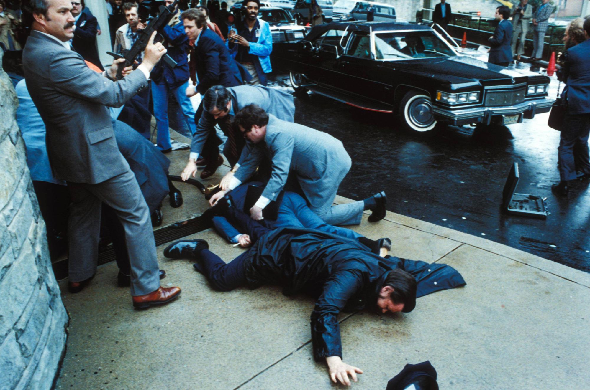 Unmittelbar nach den Schüssen auf US-Präsident Ronald Reagan überwältigen Sicherheitskräfte den Attentäter John Hinckley Jr. vor dem Washington Hilton Hotel, während der schwer verletzte Regierungssprecher James Brady und ein Polizist am Boden liegen.