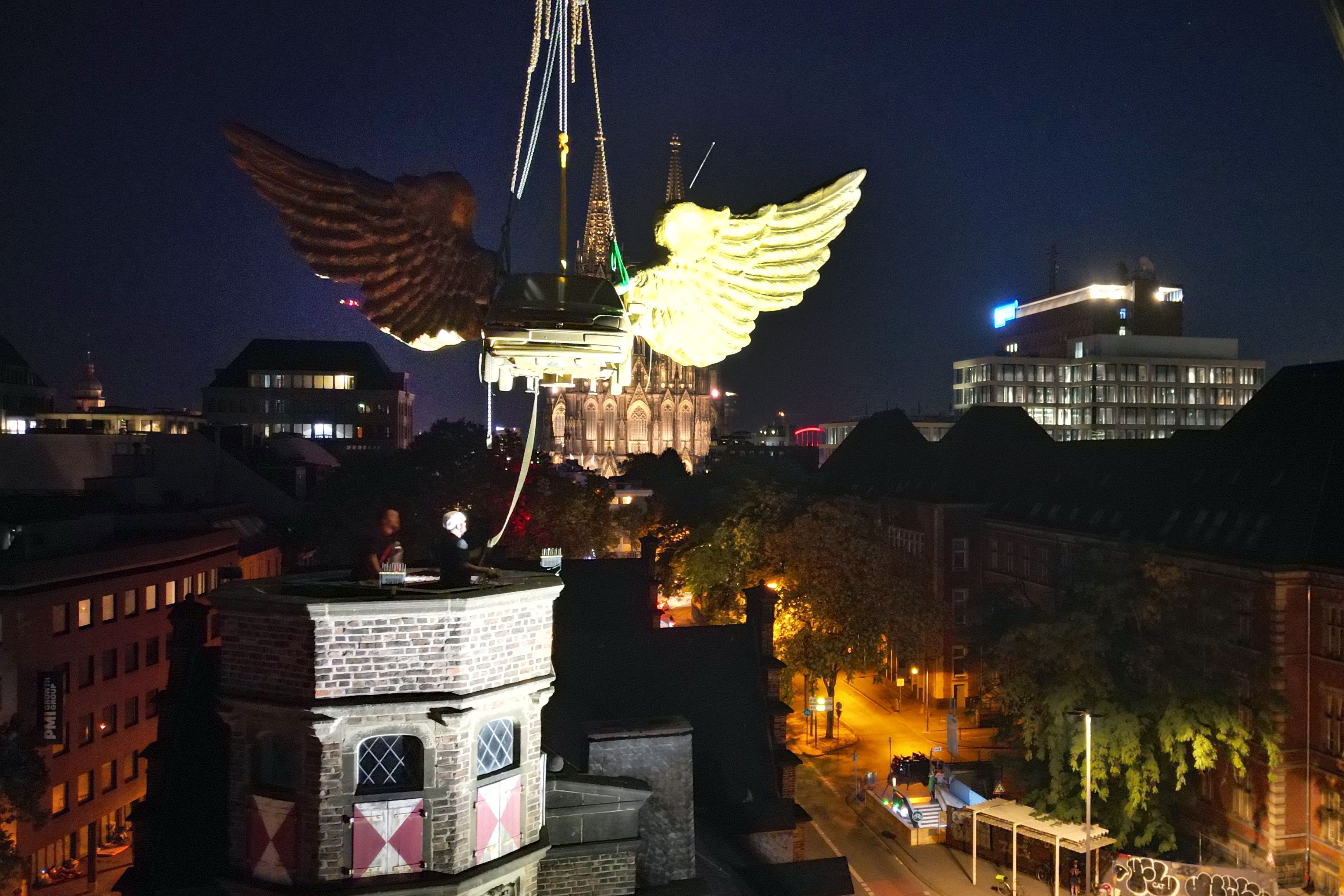 Das goldene Flügelauto des Kölner Künstlers HA Schult wird von einem Kran vom Turm des historischen Zeughauses gehoben.