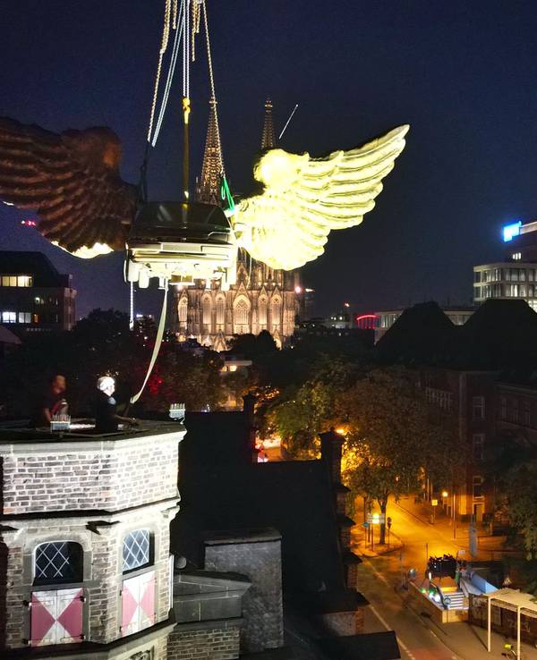 Das goldene Flügelauto des Kölner Künstlers HA Schult wird von einem Kran vom Turm des historischen Zeughauses gehoben.