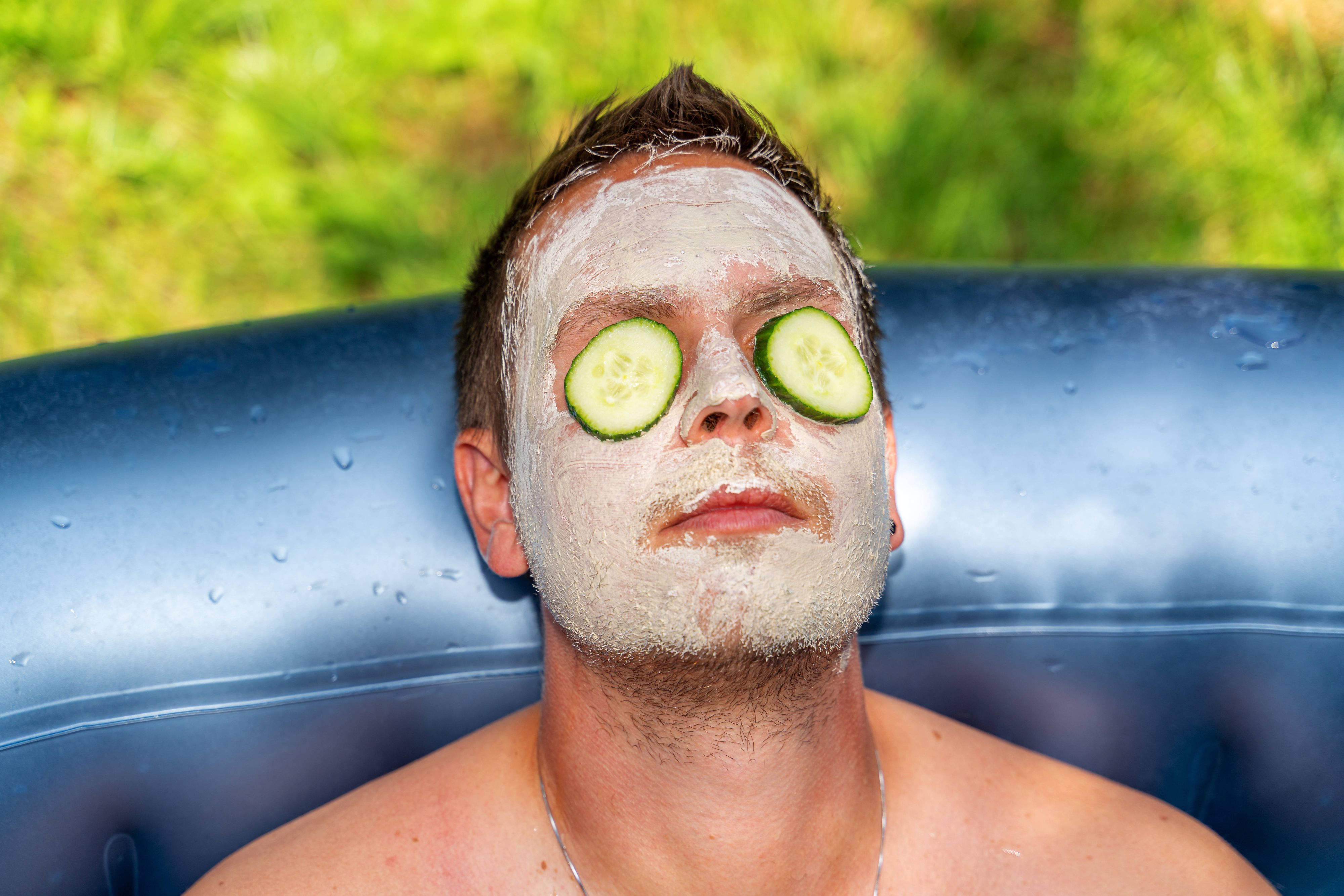 Mann mit Gurken und Gesichtsmaske aus Schlamm im Gesicht