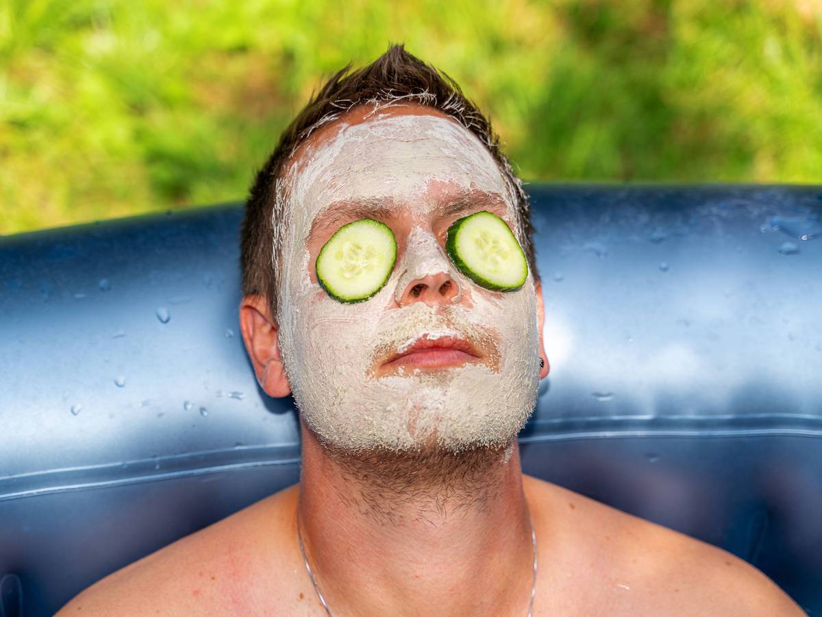 Mann mit Gurken und Gesichtsmaske aus Schlamm im Gesicht