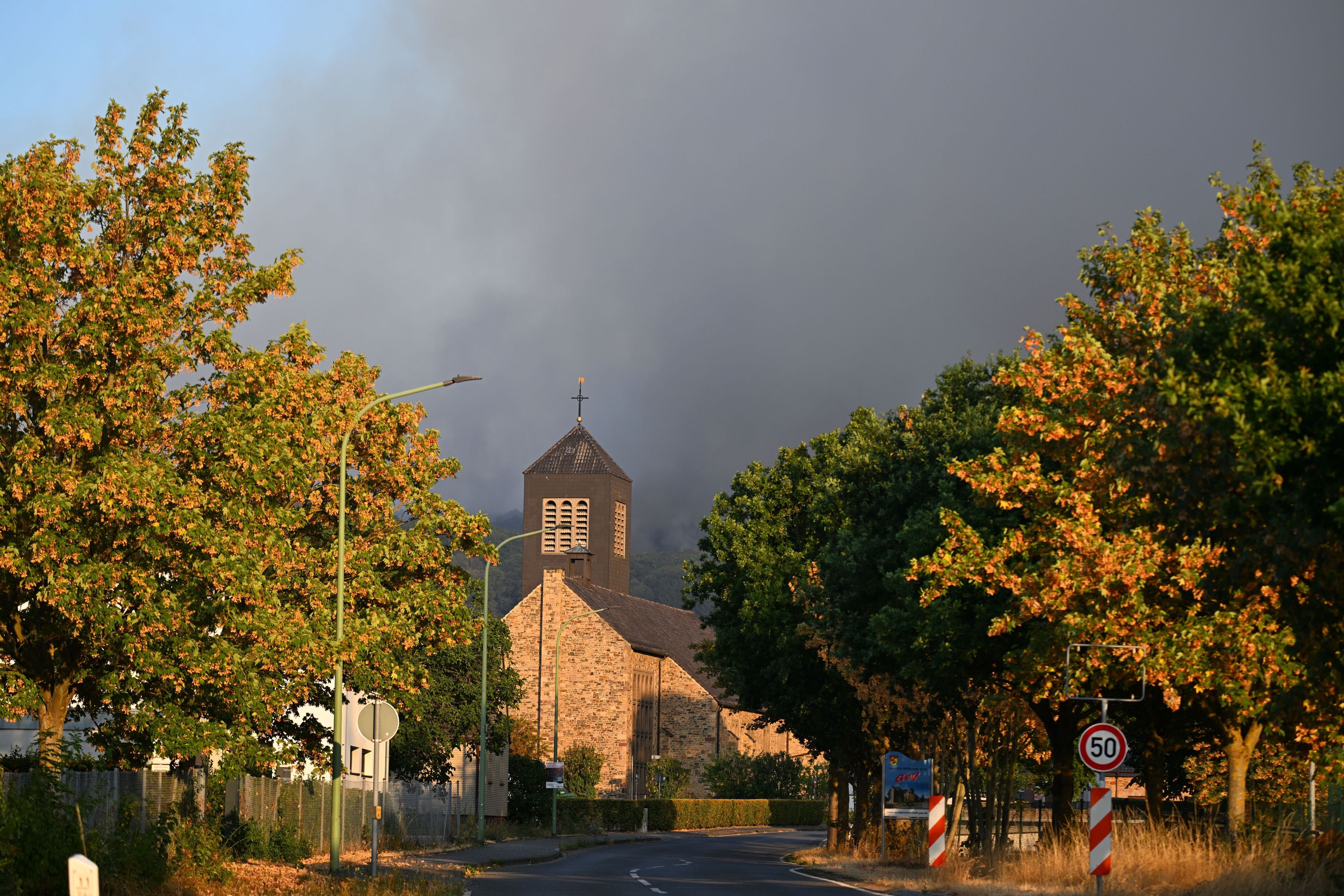 Dichter Rauch eines Waldbrands im Hürtgenwald steigt hinter der Kirche des Ortsteils Gey auf.