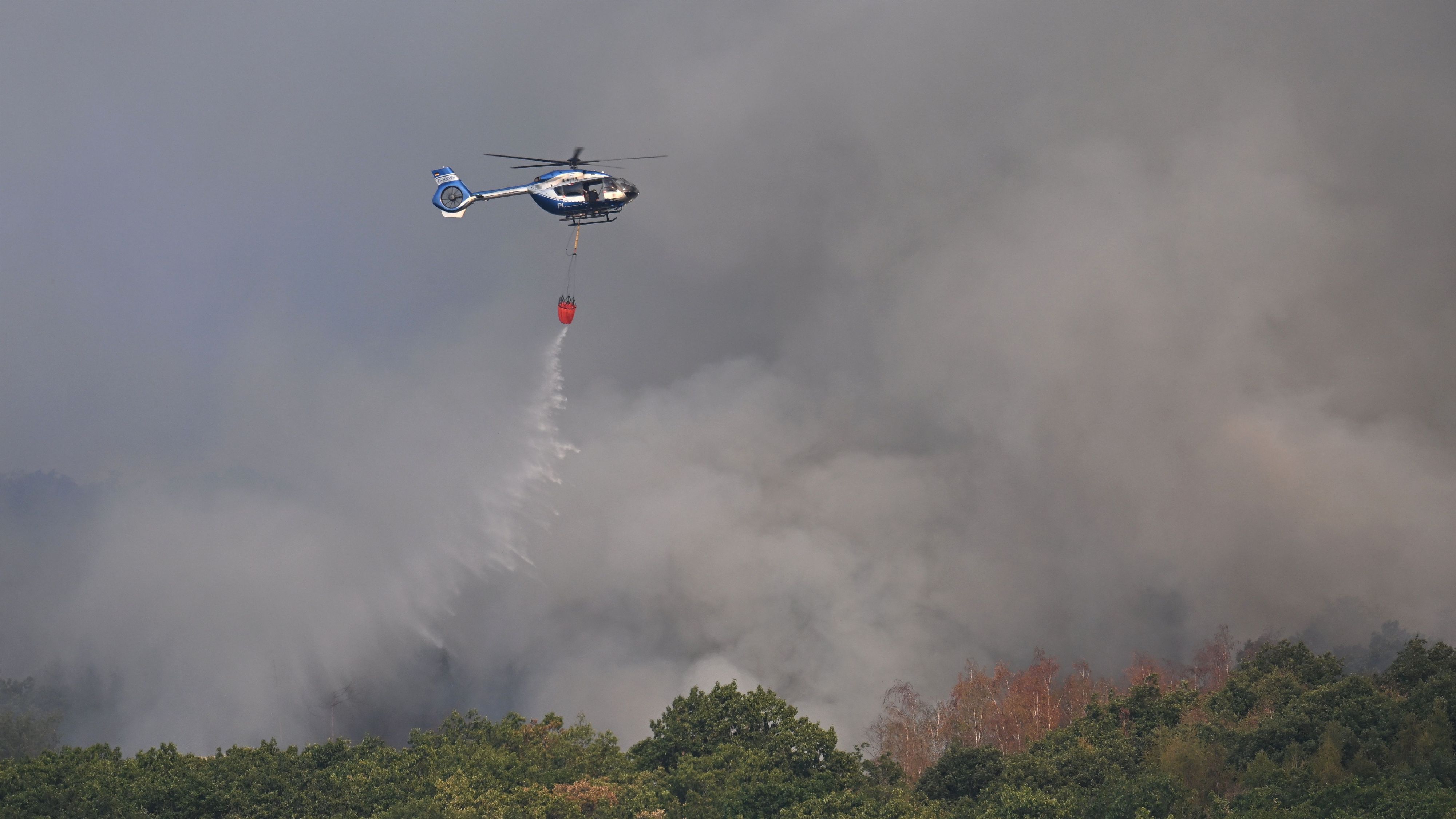 Ein Polizeihubschrauber mit Löschwasser-Außenlastbehälter unterstützt die Löscharbeiten beim Waldbrand im Hürtgenwald.