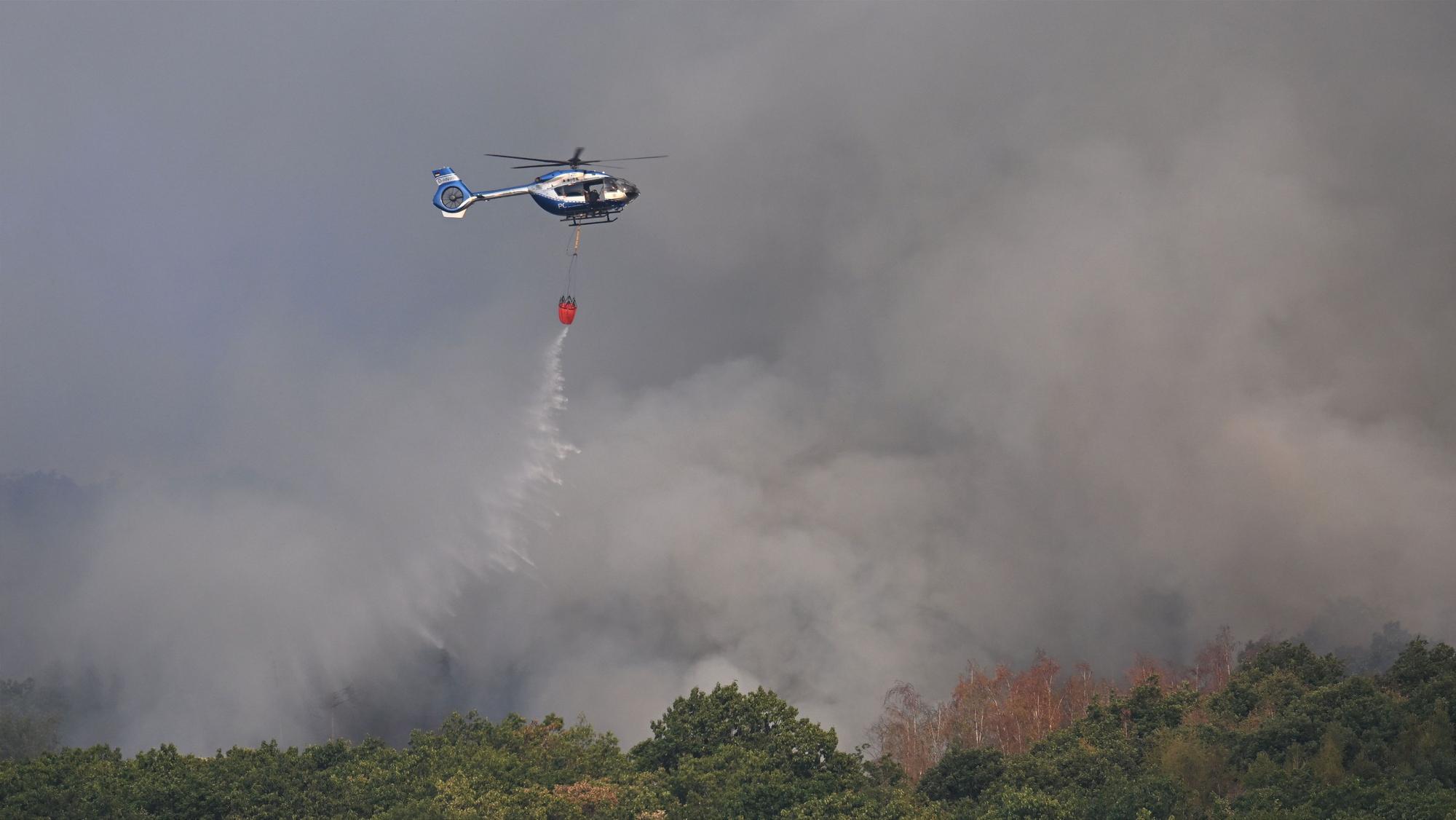 Ein Polizeihubschrauber mit Löschwasser-Außenlastbehälter unterstützt die Löscharbeiten beim Waldbrand im Hürtgenwald.