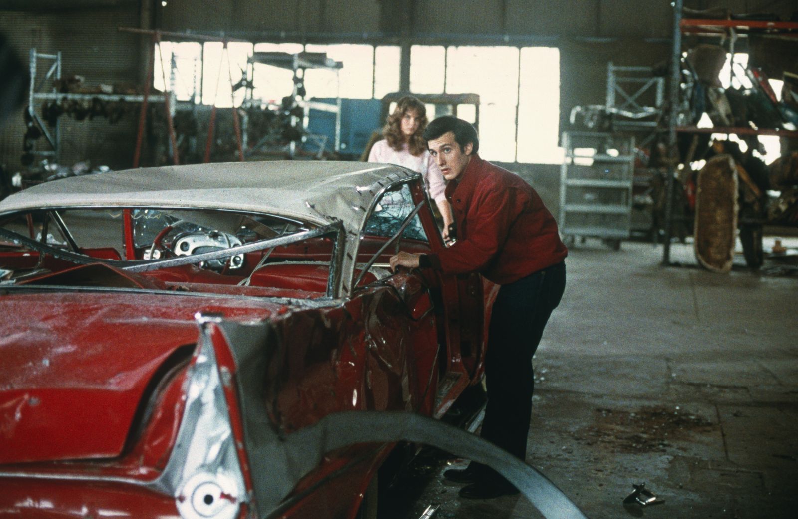 Arnie (Keith Gordon) und Leigh (Alexandra Paul) entdecken die völlig demolierte Christine in einer Werkstadt. (Bild: ZDF/© 1983 Columbia Pictures Industries, Inc. All Rights Reserved)