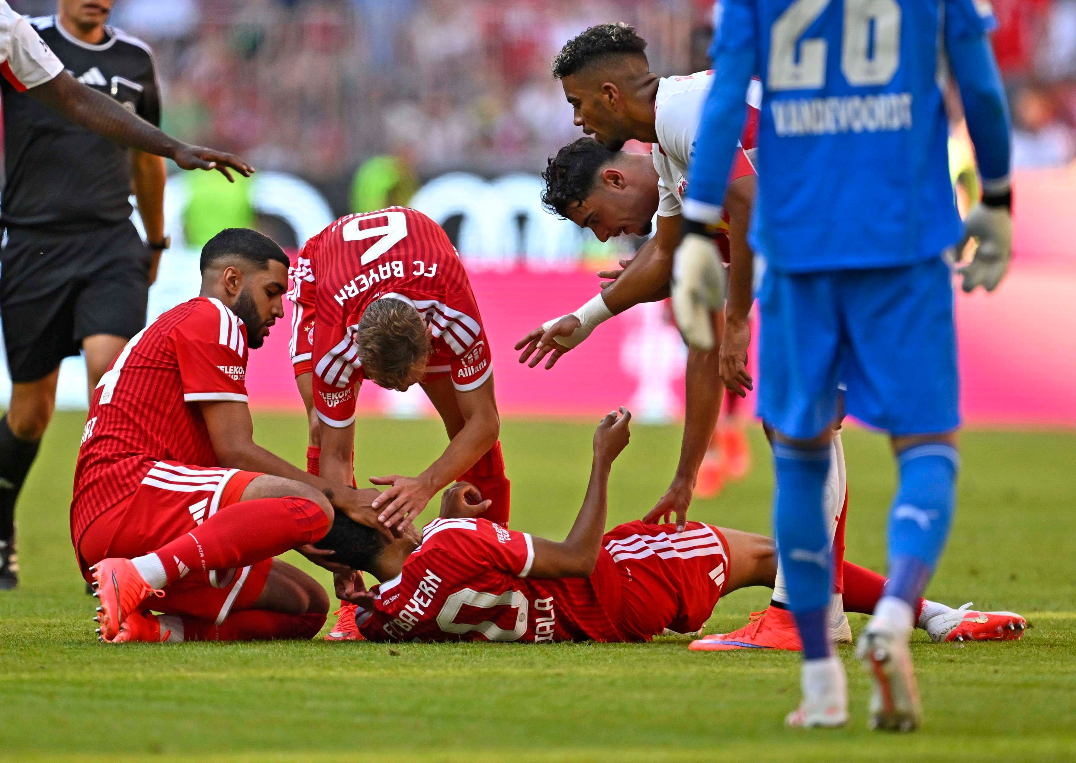 Jamal Musiala liegt auf dem Rasen, Ismael Saibari und Joshua Kimmich kümmern sich um ihn.