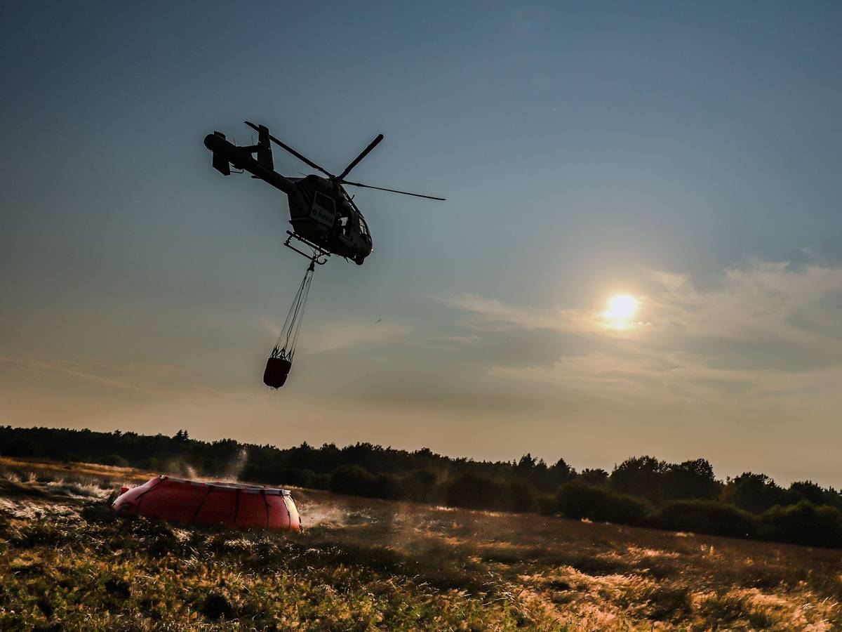 Ein Hubschrauber der belgischen Polizei mit einem Bambi Bucket, ein Löschwasser-Außenlastbehälter, fliegt zu einer provisorischen Wasseraufladestelle im Hohen Venn, um Löschwasser aufzutanken.
