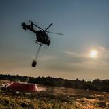 Ein Hubschrauber der belgischen Polizei mit einem Bambi Bucket, ein Löschwasser-Außenlastbehälter, fliegt zu einer provisorischen Wasseraufladestelle im Hohen Venn, um Löschwasser aufzutanken.