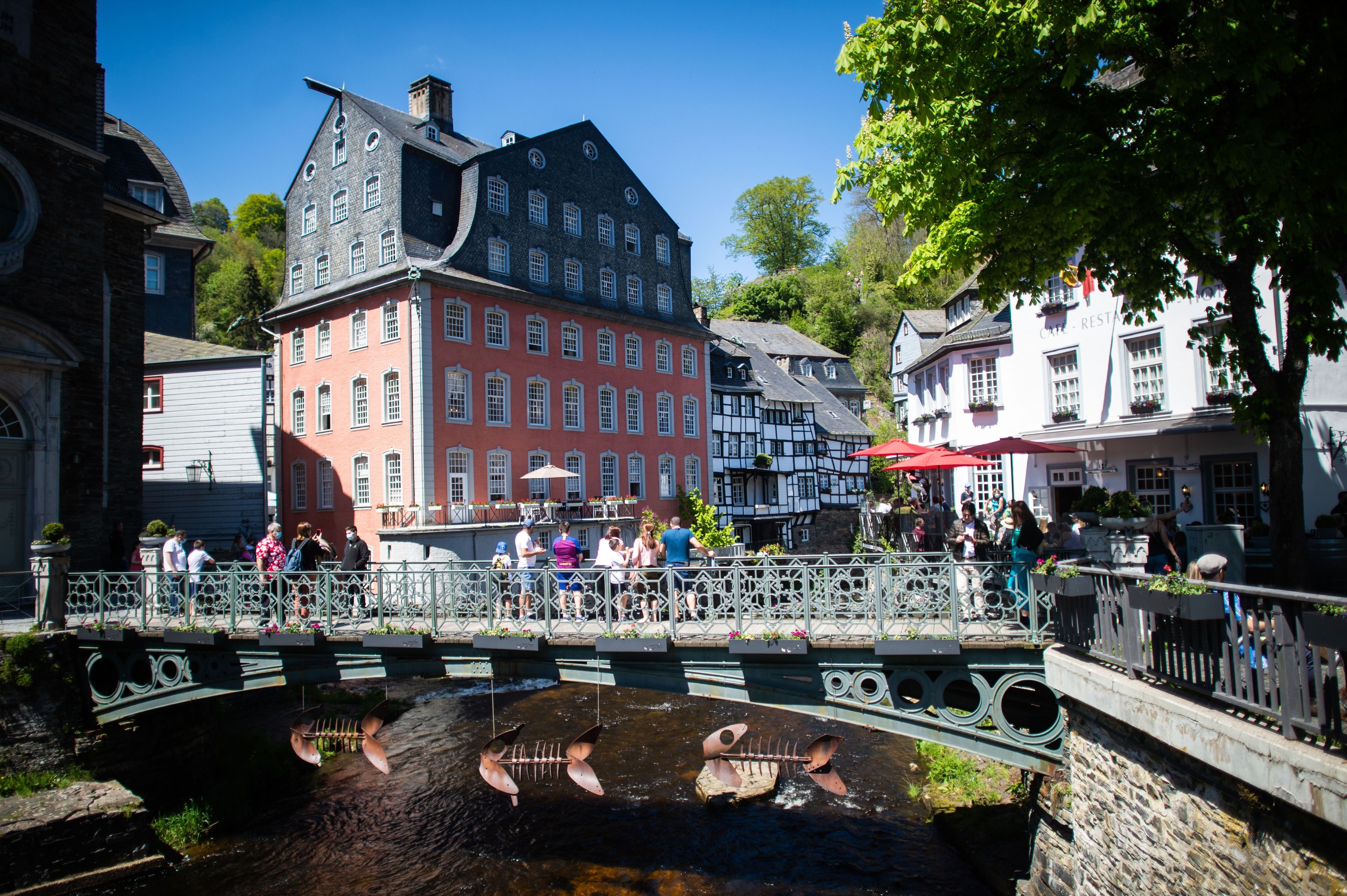 Menschen stehen auf einer Brücke vor dem so genannten „Roten Haus“. Meteorologen sagen für den heutigen Sonntag und die kommenden Tage viel Sonne und warme Temperaturen voraus.