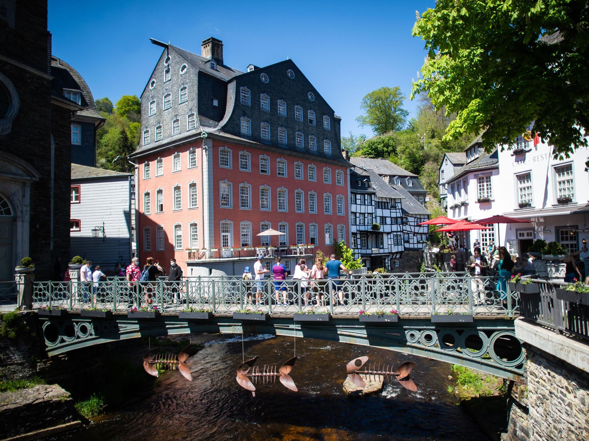 Menschen stehen auf einer Brücke vor dem so genannten „Roten Haus“. Meteorologen sagen für den heutigen Sonntag und die kommenden Tage viel Sonne und warme Temperaturen voraus.