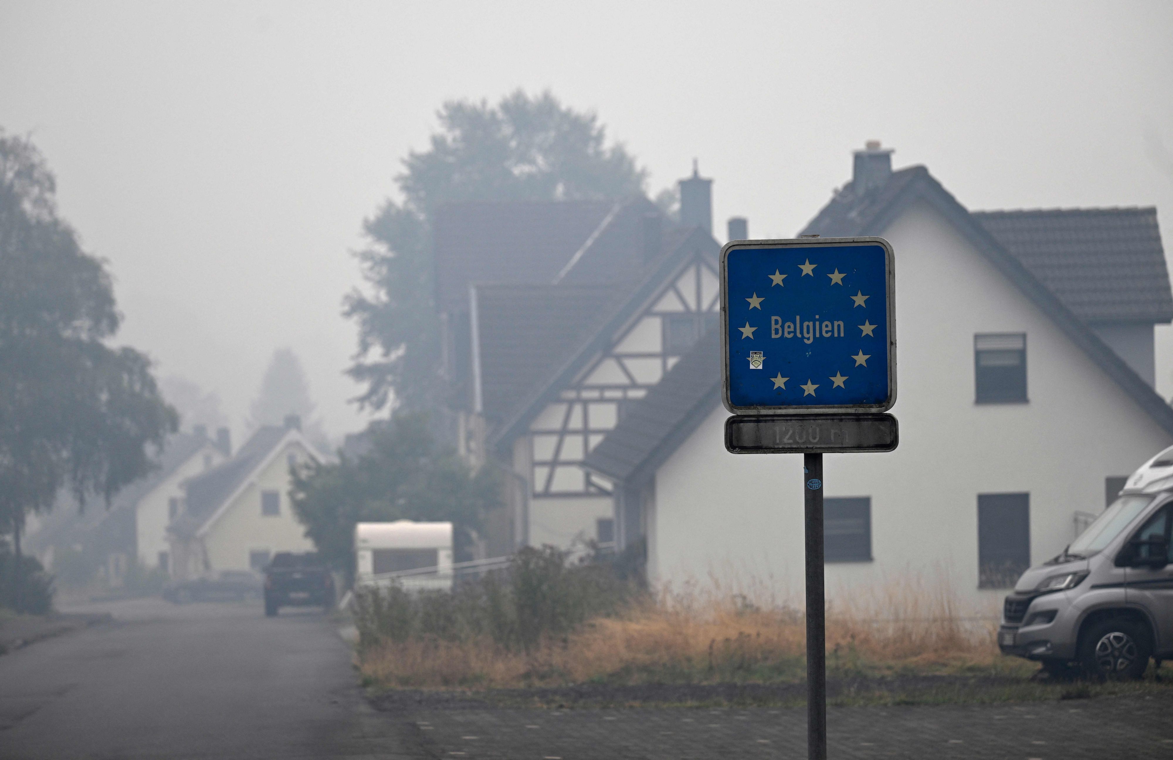 Auf dem Foto ist ein Wegweiser zur belgischen Grenze zu sehen, während am 17. August 2026 Rauch über den Häusern in Kalterherberg bei Monschau in Westdeutschland hängt.