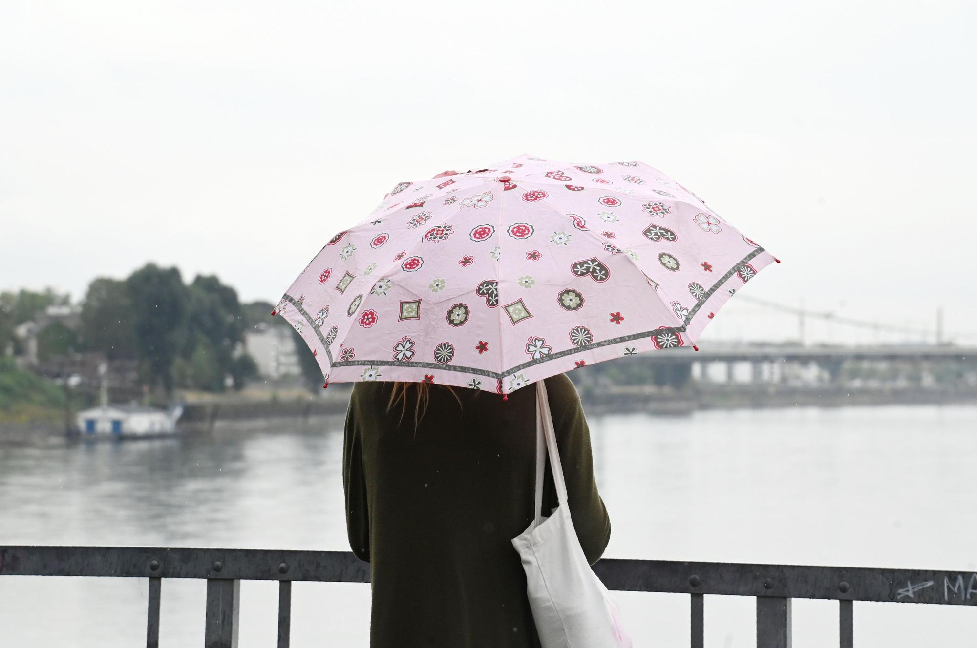 Eine Frau mit Regenschirm steht vor dem Rhein