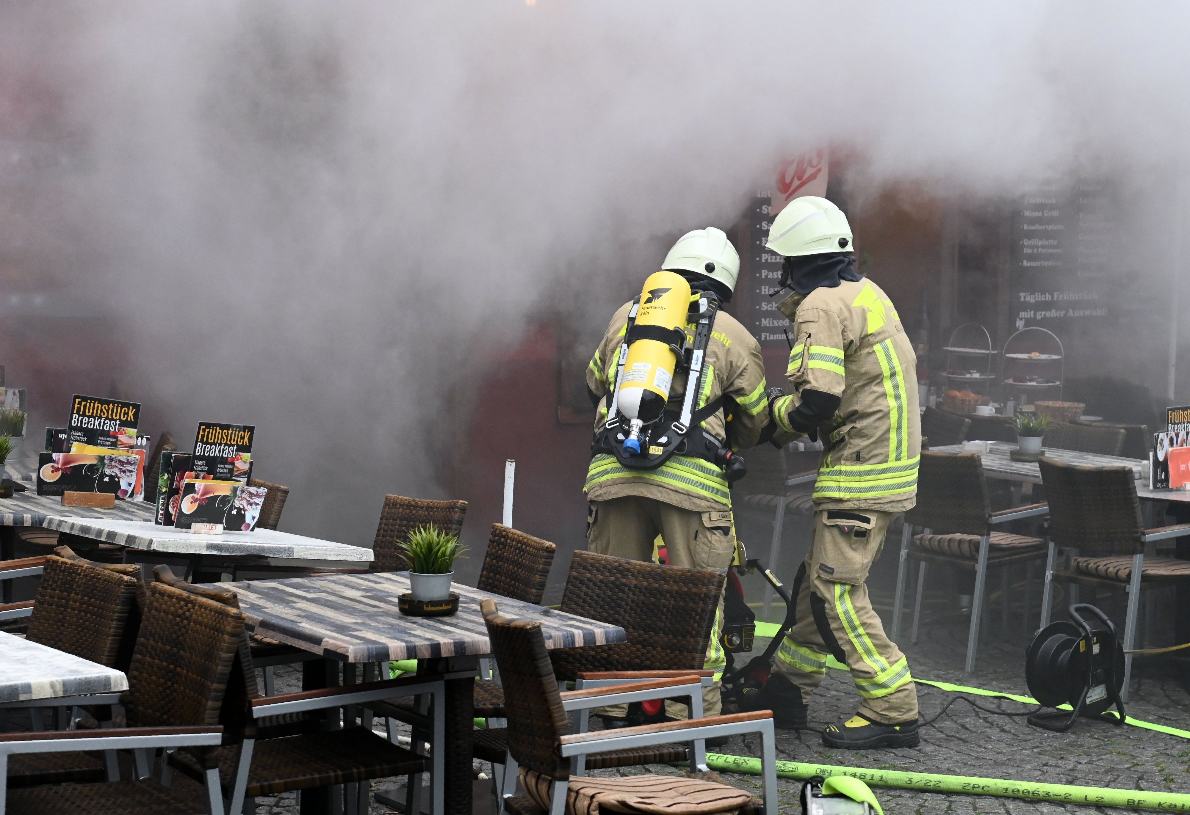 Aus einem Gebäude dringt dichter Qualm, in dem zwei Feuerwehrleute löschen.
