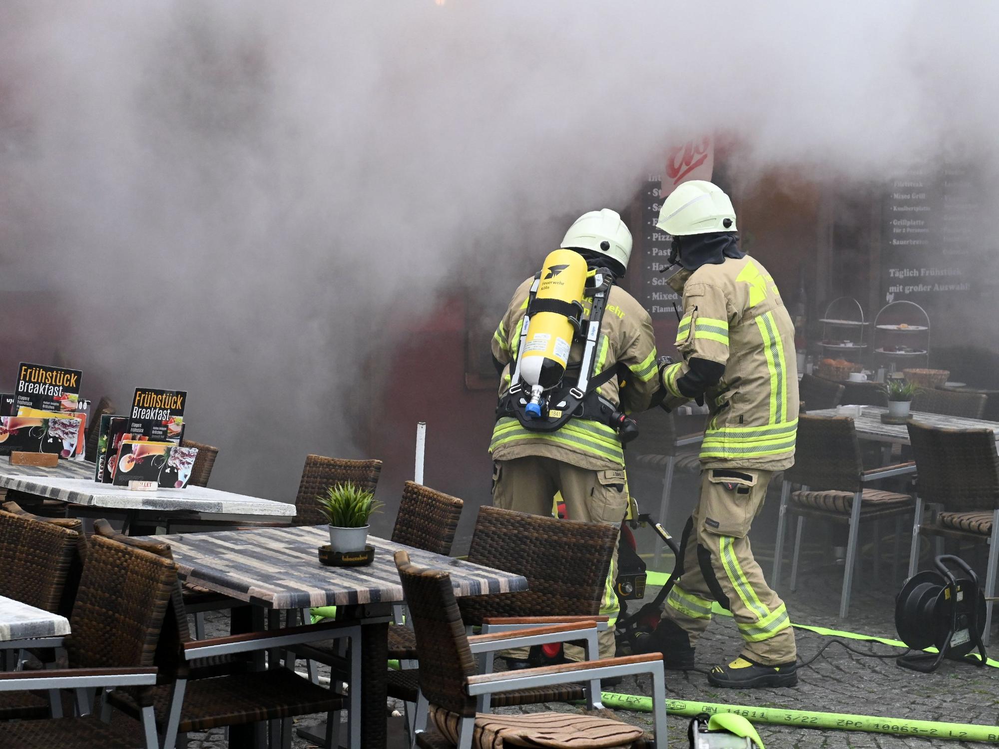 Aus einem Gebäude dringt dichter Qualm, in dem zwei Feuerwehrleute löschen.
