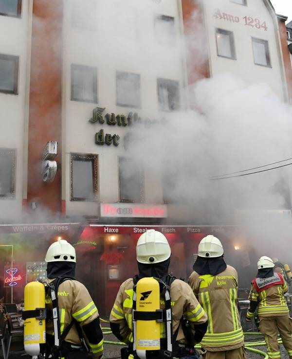 Feuerwehrleute stehen vor einem Gebäude, aus dem dichter Qualm dringt.