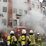 Feuerwehrleute stehen vor einem Gebäude, aus dem dichter Qualm dringt.