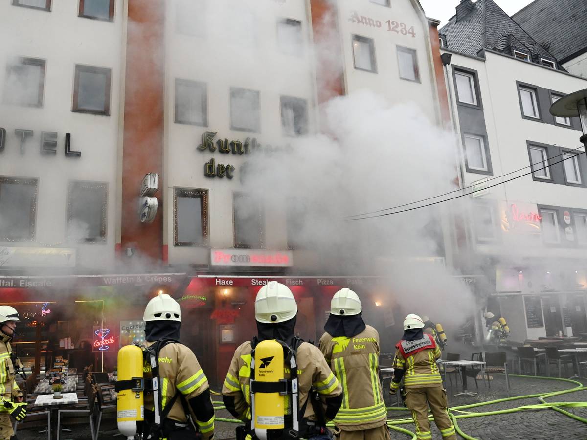 Feuerwehrleute stehen vor einem Gebäude, aus dem dichter Qualm dringt.