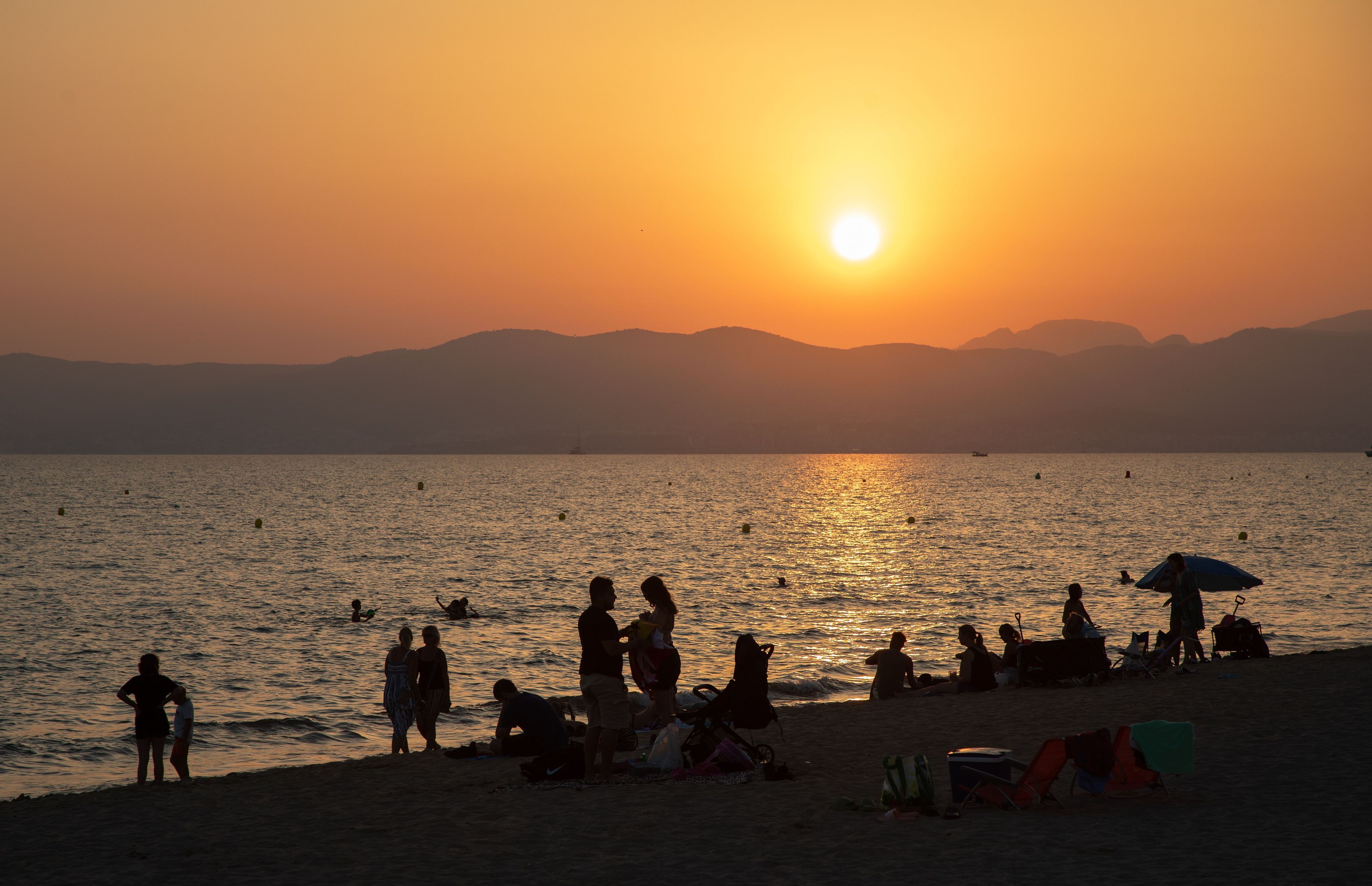 Am Strand von Playa de Palma auf Mallorca baden Menschen bei Sonnenuntergang im Meer.