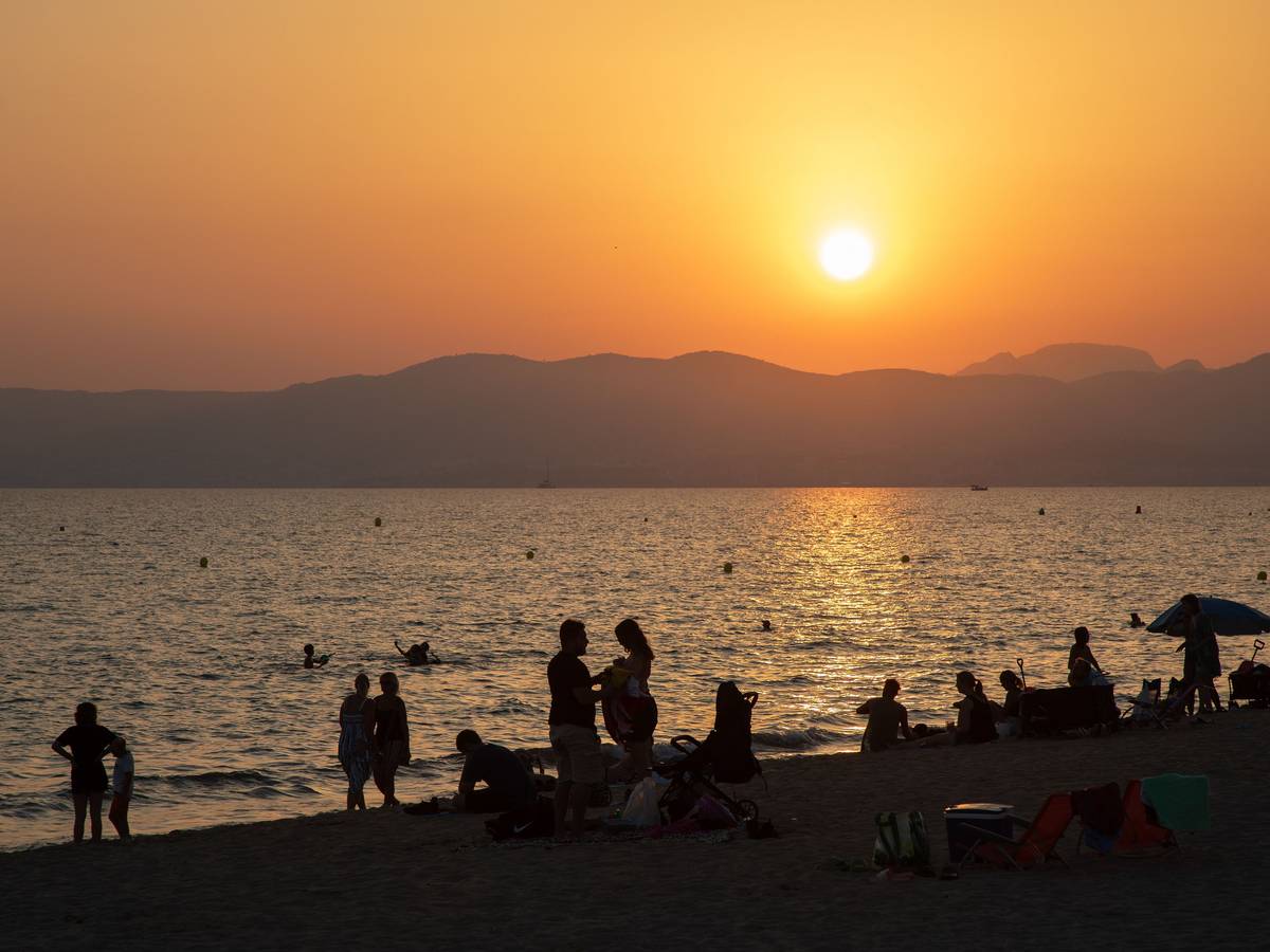 Am Strand von Playa de Palma auf Mallorca baden Menschen bei Sonnenuntergang im Meer.