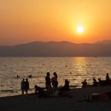 Am Strand von Playa de Palma auf Mallorca baden Menschen bei Sonnenuntergang im Meer.