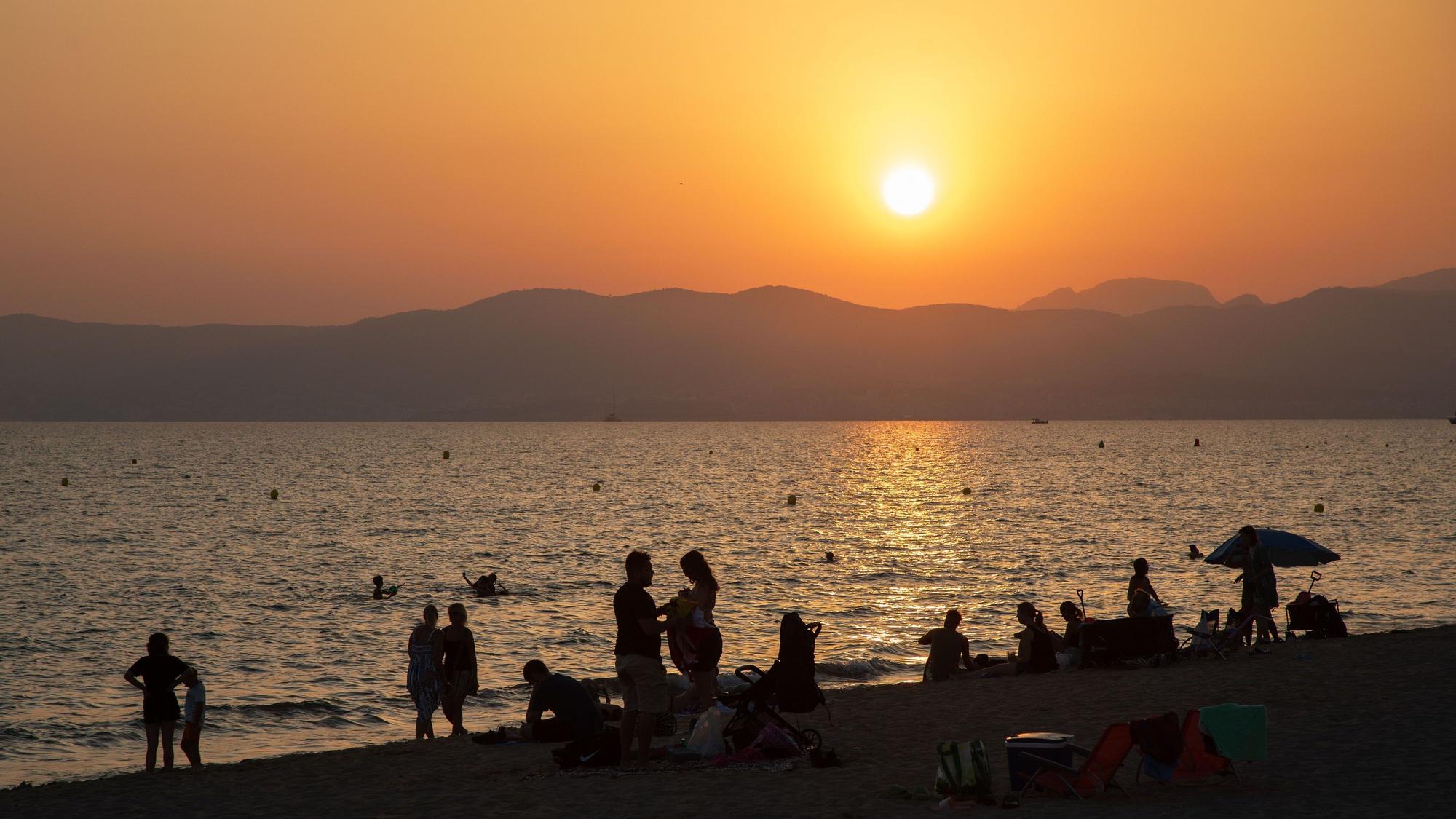 Am Strand von Playa de Palma auf Mallorca baden Menschen bei Sonnenuntergang im Meer.