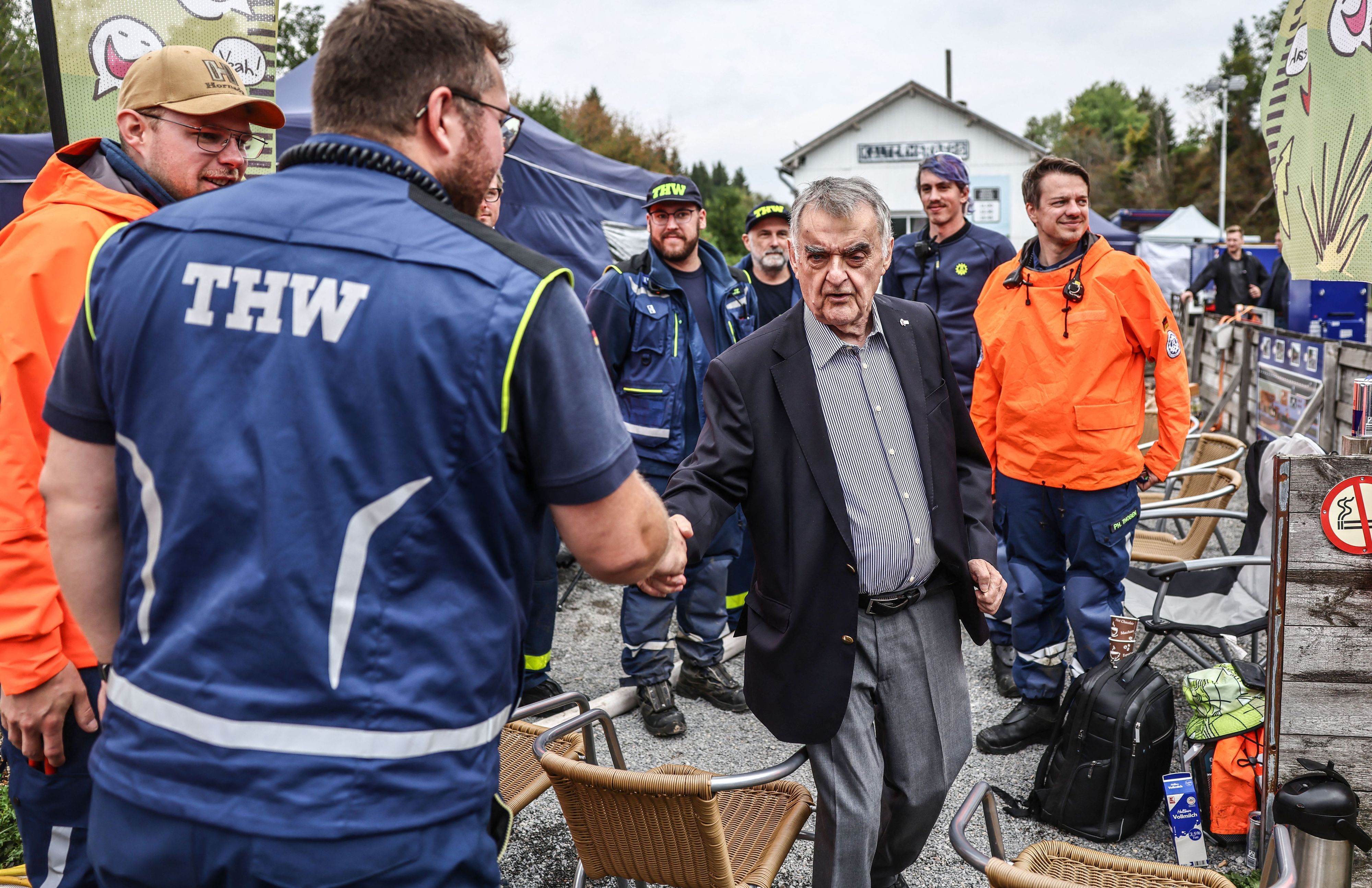 NRW-Innenminister Herbert Reul (Mitte, CDU) spricht mit Helfern des THW an der deutsch-belgischen Grenze an einer Wassertankstation.