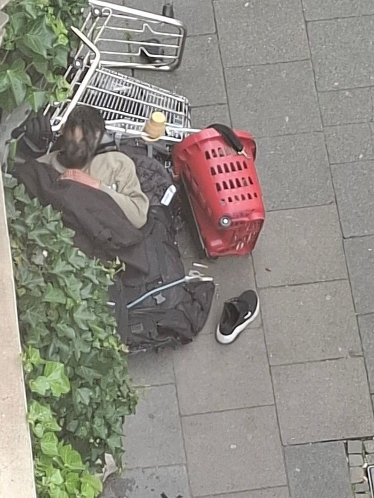 Ein Mann schläft auf dem Gehweg, den Kopf auf einem umgekippten Einkaufswagen.