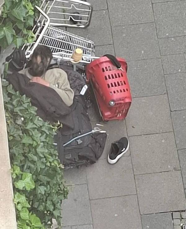 Ein Mann schläft auf dem Gehweg, den Kopf auf einem umgekippten Einkaufswagen.
