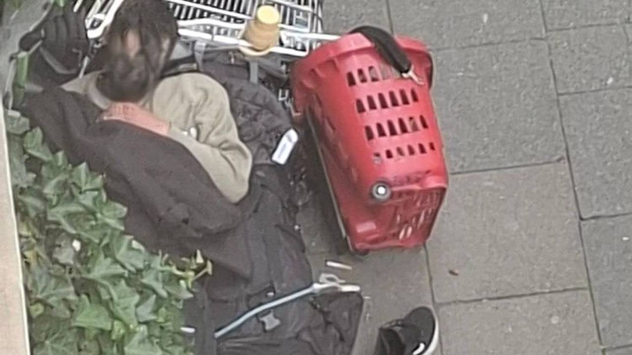 Ein Mann schläft auf dem Gehweg, den Kopf auf einem umgekippten Einkaufswagen.