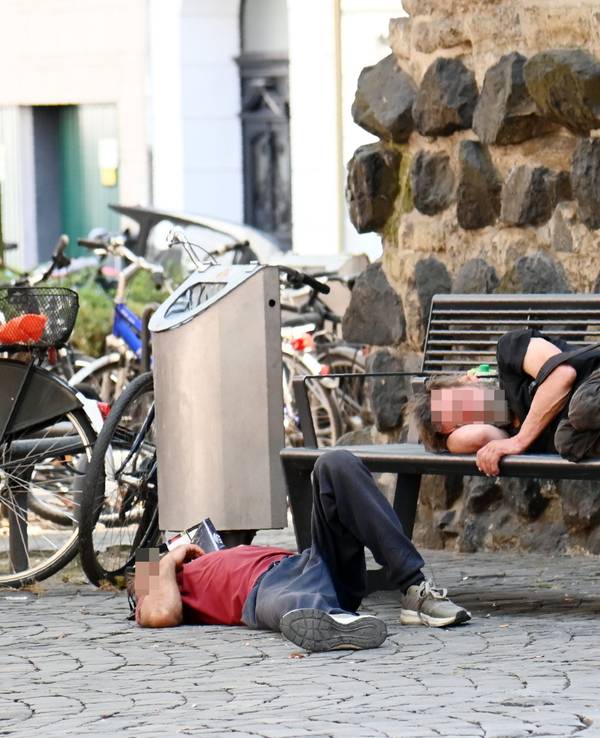 Obdachlose liegen an der Eigelsteintorburg auf und vor einer Sitzbank.