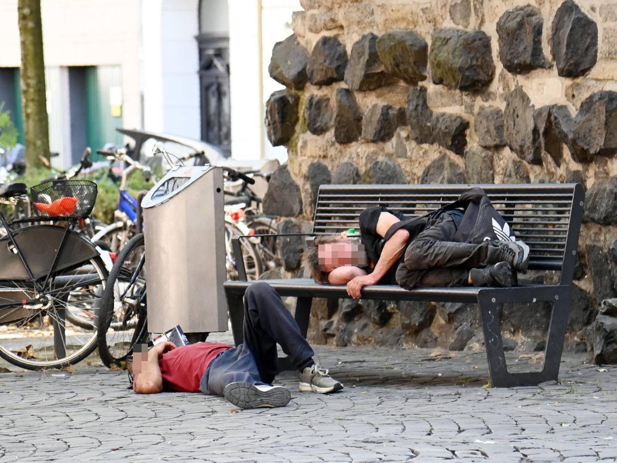 Obdachlose liegen an der Eigelsteintorburg auf und vor einer Sitzbank.