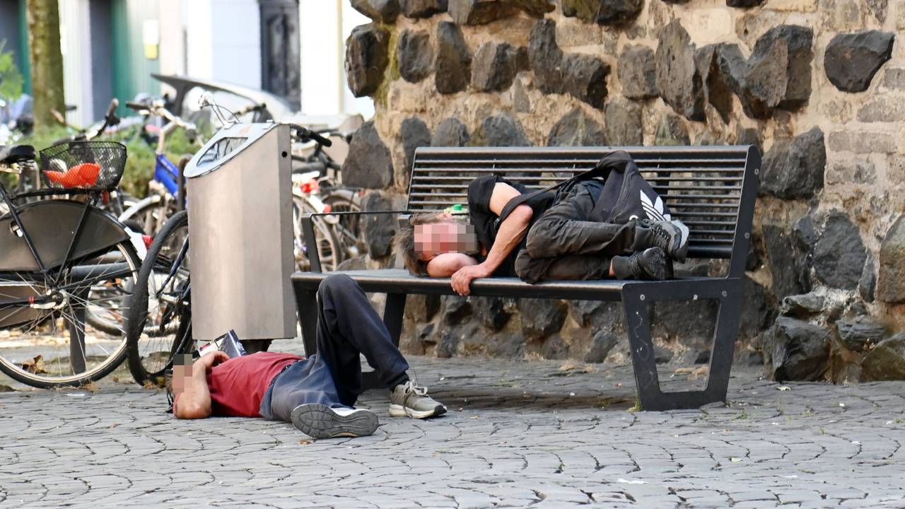 Obdachlose liegen an der Eigelsteintorburg auf und vor einer Sitzbank.