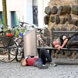 Obdachlose liegen an der Eigelsteintorburg auf und vor einer Sitzbank.