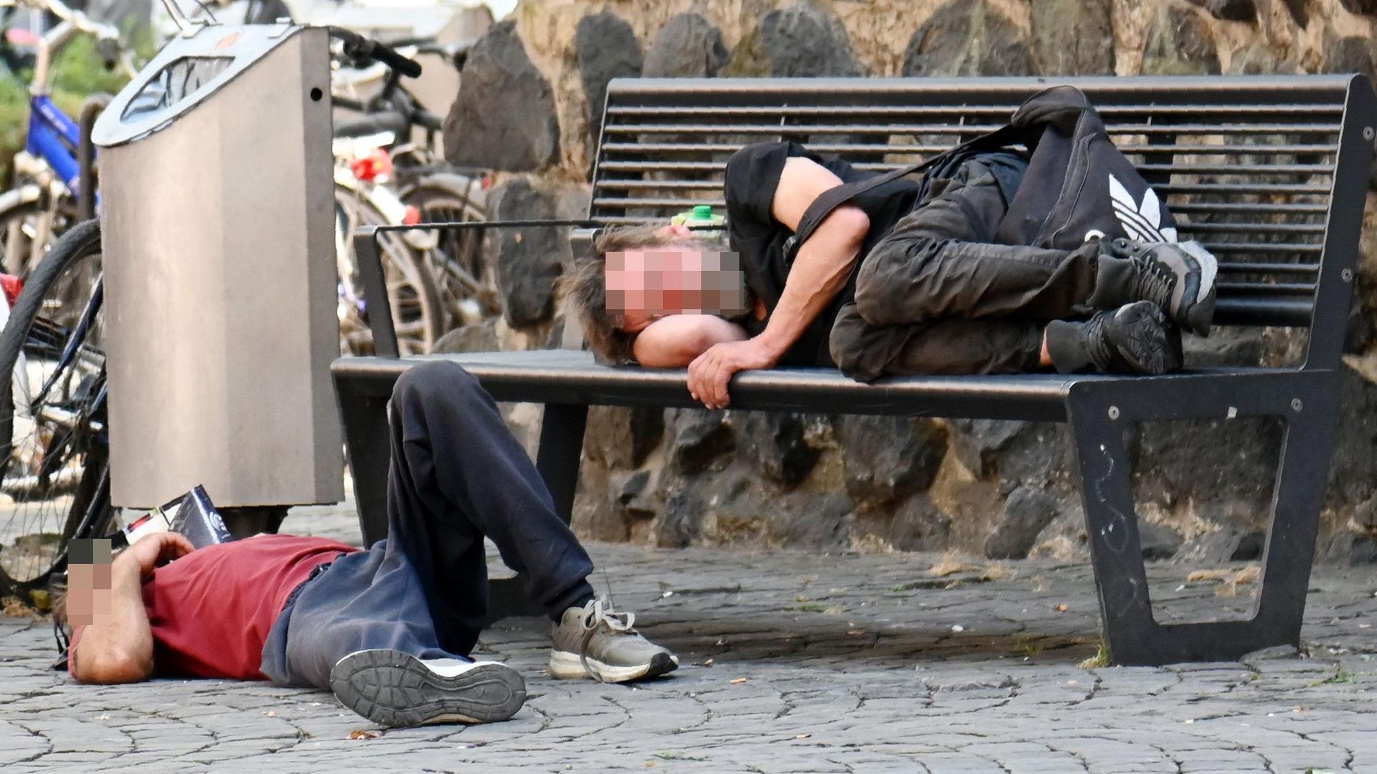 Obdachlose liegen an der Eigelsteintorburg auf und vor einer Sitzbank.