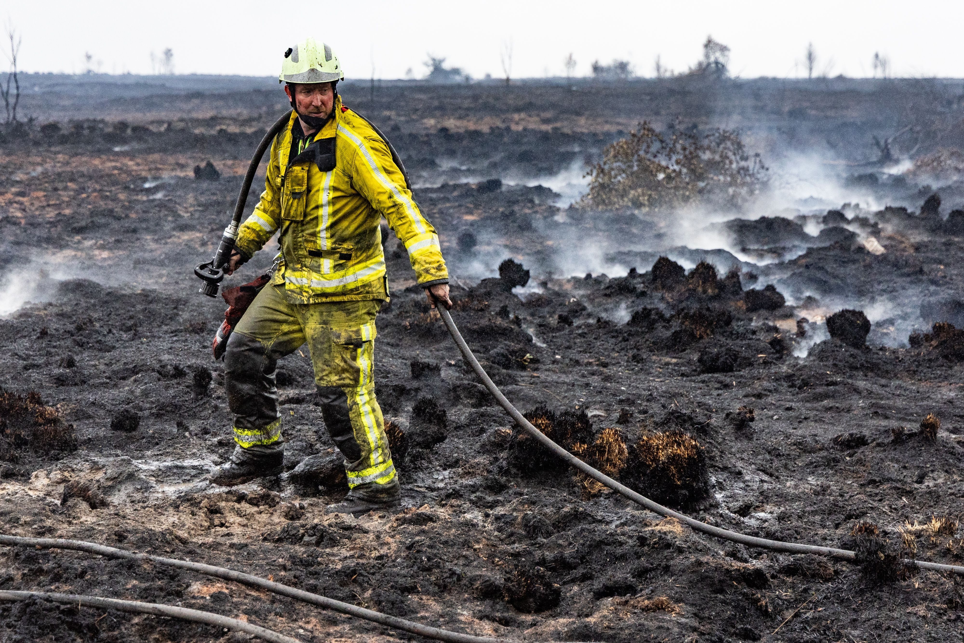 Ein Feuerwehrmann löscht Glutnester im schwelenden Boden.