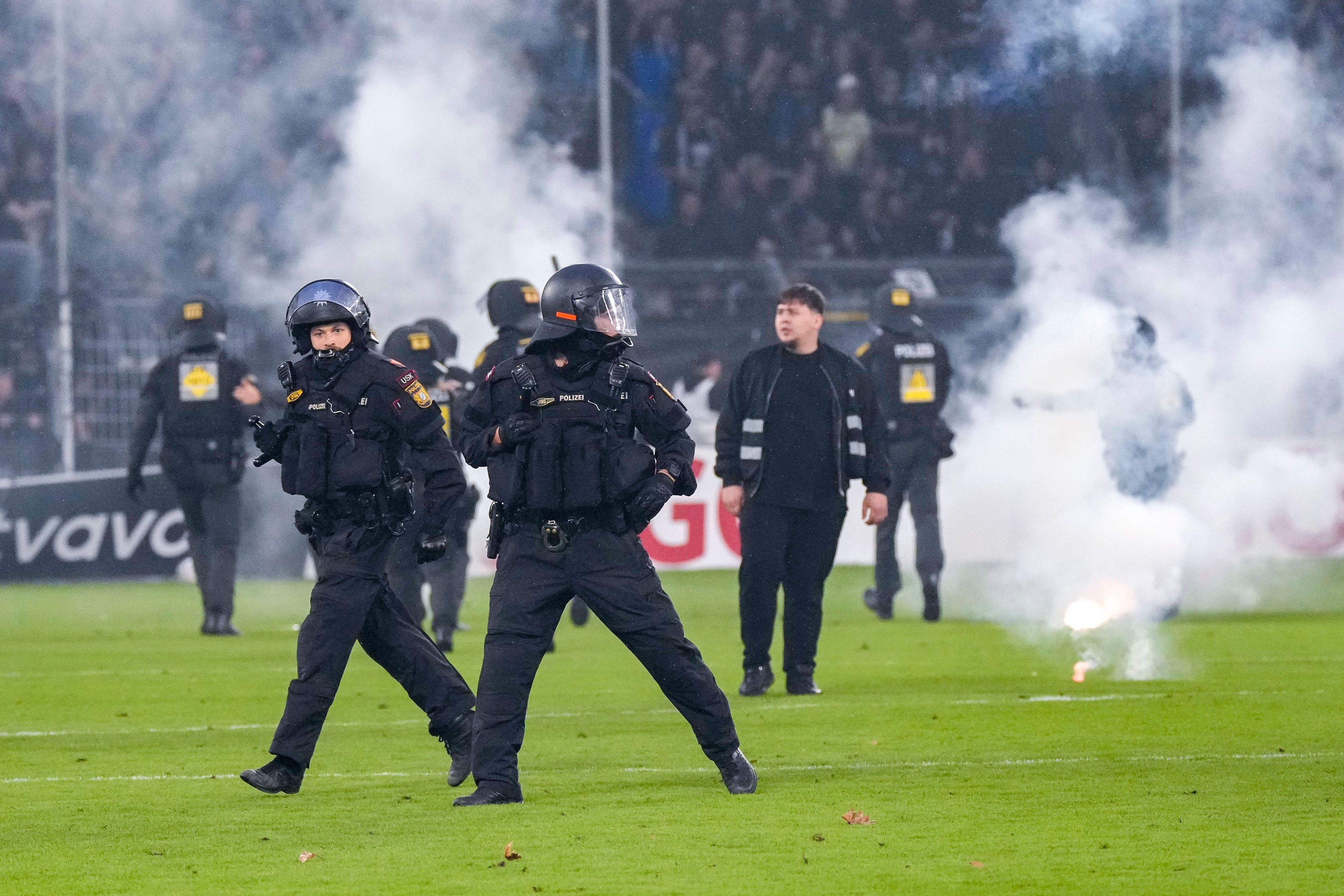 Polizisten sichern das Spielfeld nach Pyroattacken von den Rängen.