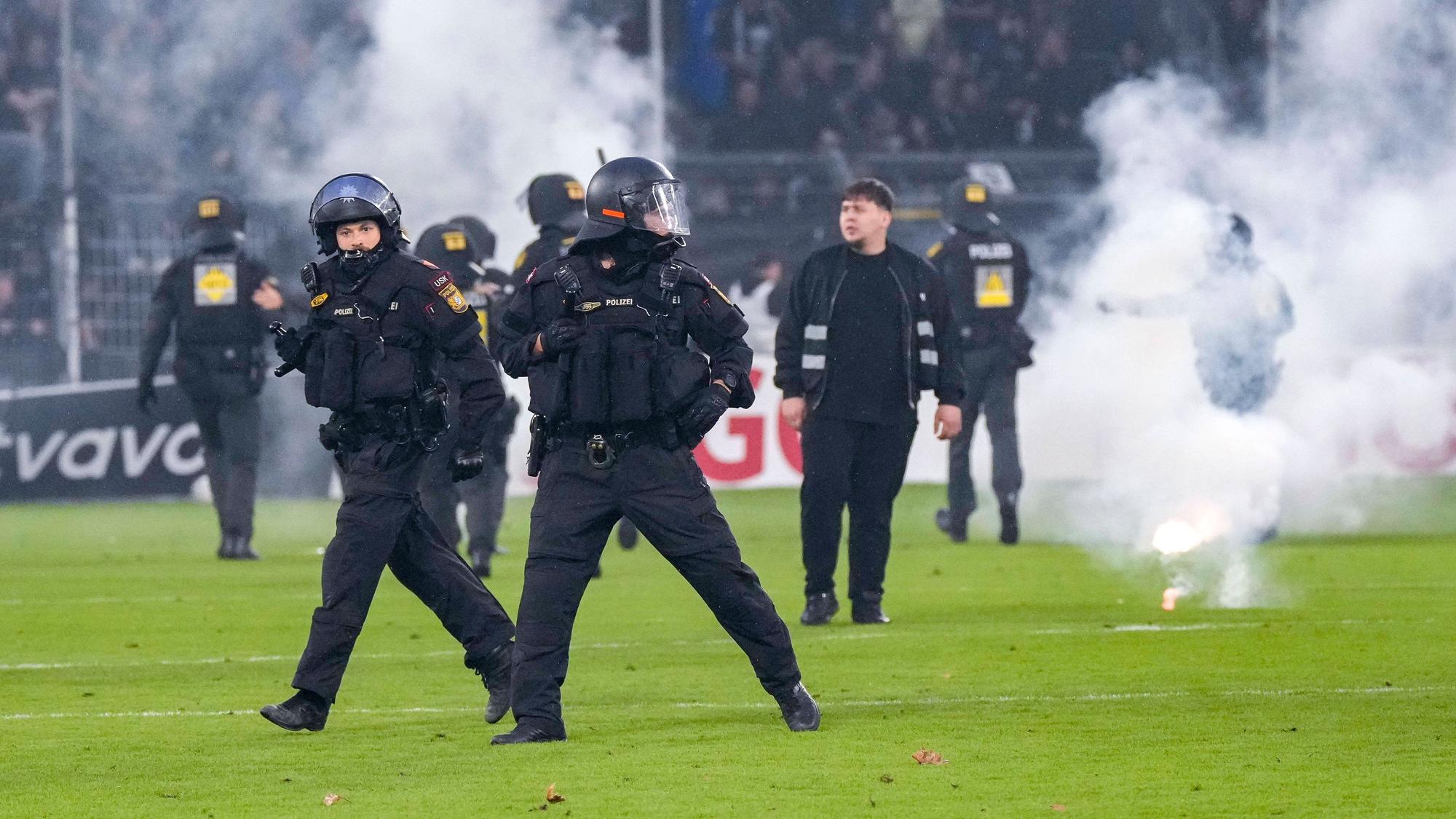 Polizisten sichern das Spielfeld nach Pyroattacken von den Rängen.