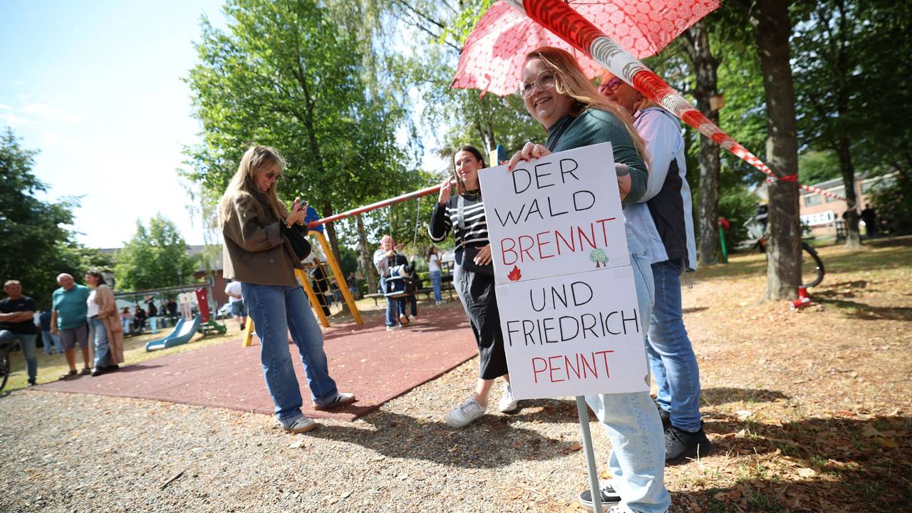 Eine Frau hält in Hürtgenwald ein Schild mit der Aufschrift „Der Wald brennt und Friedrich pennt“ vor dem Besuch von Bundeskanzler Merz in Hürtgenwald-Gey. Zwei Tage nach der vollständigen Löschung des verheerenden Waldbrands in der Eifel besucht Bundeskanzler das Gebiet, um den Helfern zu danken