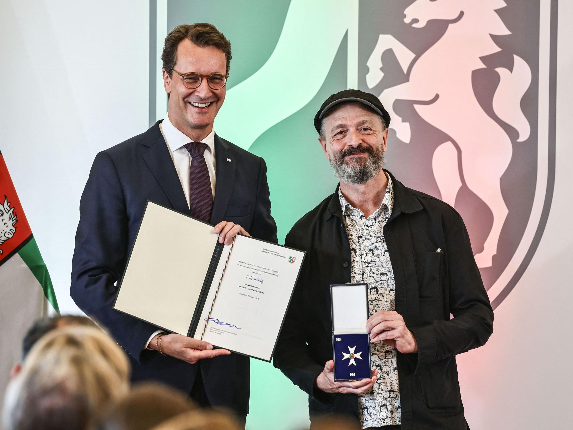 Ralf König nimmt von Hendrik Wüst den Landesverdienstorden entgegen.