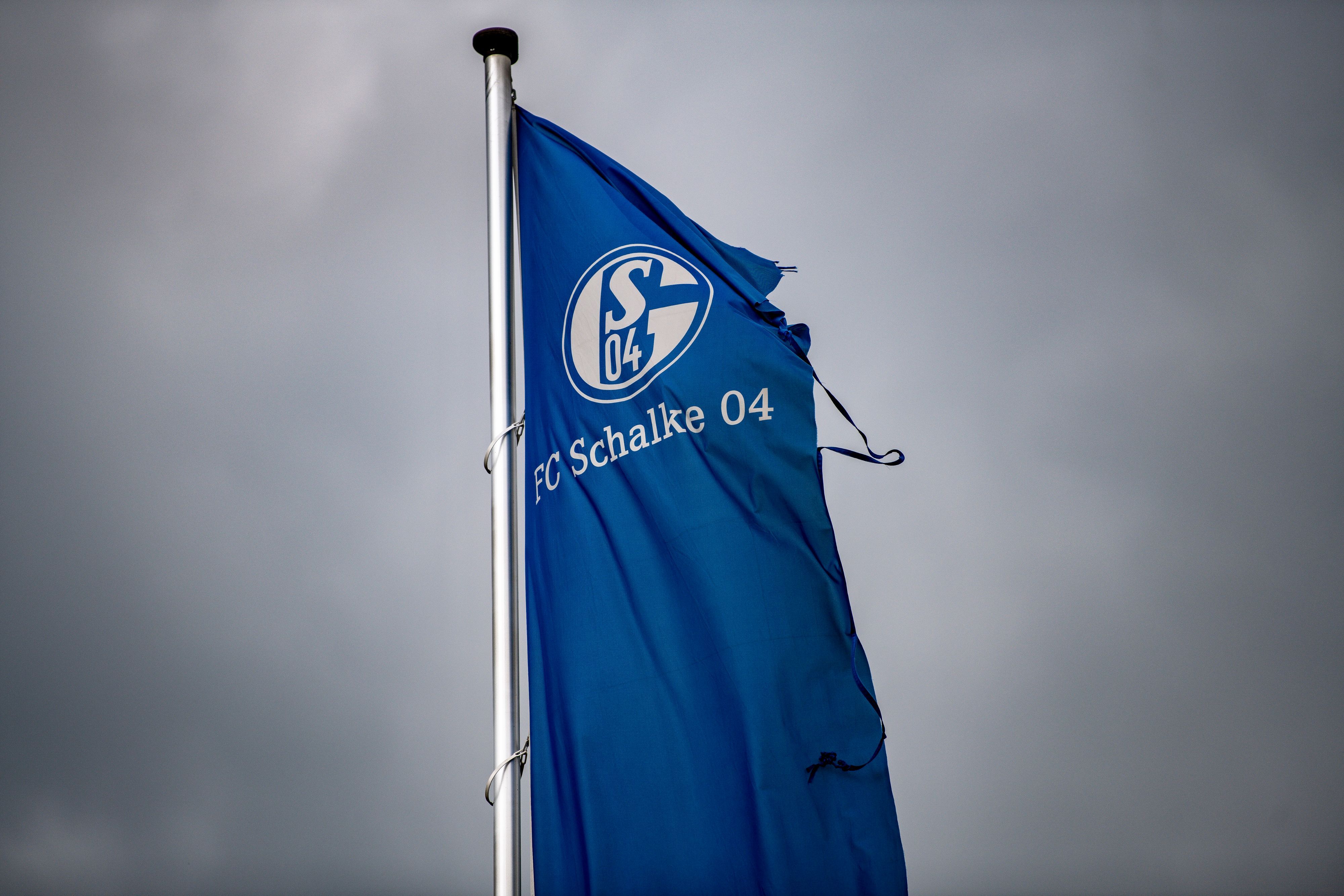 Eine zerrissene Schalke-Fahne weht über der Veltins-Arena in Gelsenkirchen mit einem dunklen Himmel im HIntergrund.