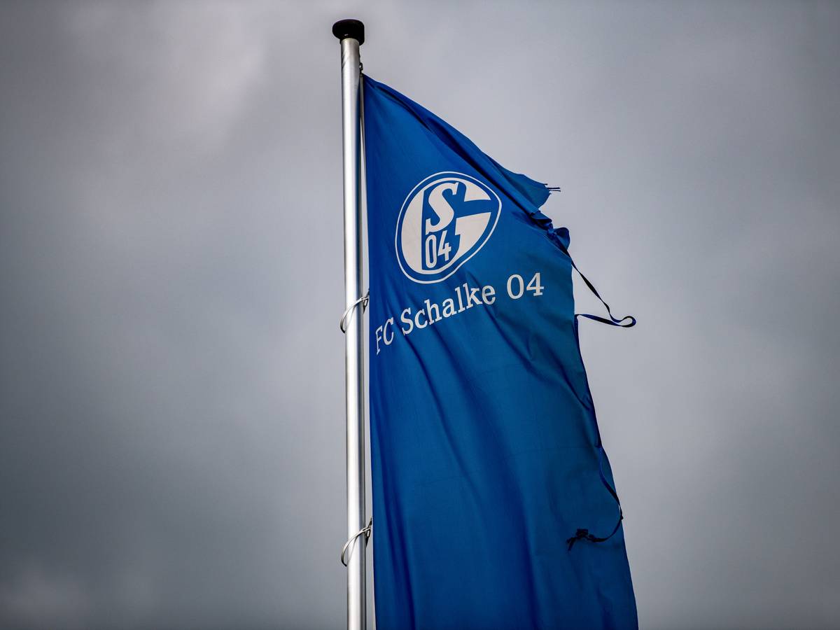 Eine zerrissene Schalke-Fahne weht über der Veltins-Arena in Gelsenkirchen mit einem dunklen Himmel im HIntergrund.