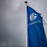 Eine zerrissene Schalke-Fahne weht über der Veltins-Arena in Gelsenkirchen mit einem dunklen Himmel im HIntergrund.